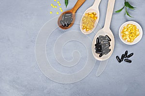 Black, yellow pill and wooden spoon on grey background