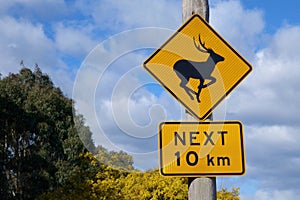 A black and yellow road sign warning that deer might be ahead for the next ten km.