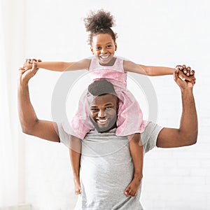 Black young dad carrying his little princess daughter on shoulders