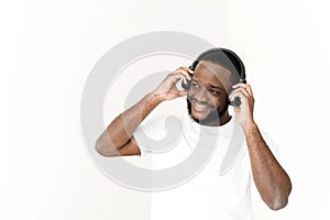 Black young man enjoying music in wireless headphones and singing at white background