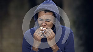 Black young man with face scar eating snack street, troubled teen, behavior
