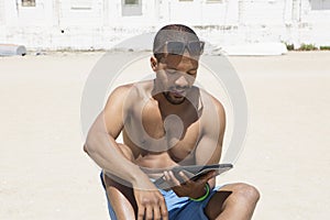Black young man feeling happy to spend his free time very well staying against blue sea and working with tablet.