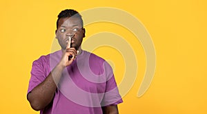 Black Young Man Gesturing Hush Sign Over Yellow Studio Background