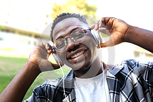 Black young man relaxing outdoors listening to music using headphones looking at camera.