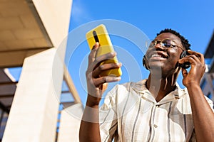 Black young man relaxing outdoors listening to music using phone and headphones. Copy space.