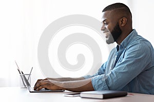 Black Young Man Using Laptop At Home, Enjoying Remote Work, Side View