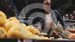 Black young woman is choosing oranges in a supermarket