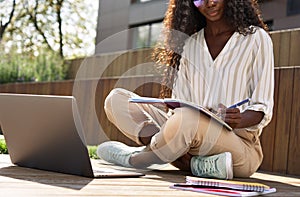 African young woman student learning using laptop studying outside campus.