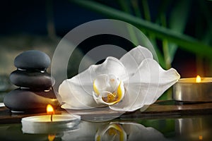Black zen stones,candles and white orchids on a wooden plank on the surface of the water. SPA, relaxation, meditation