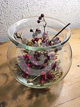 Blackberries, holly, rosehip and grasses in glass vase decorated autumnally