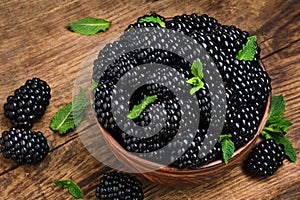 Blackberries and leaves of green mint in bowl on wood background