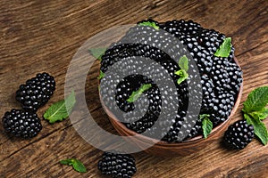 Blackberries and leaves of green mint in bowl on wood background