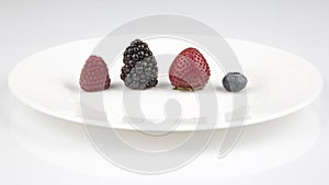 Blackberries, raspberries, blueberries and strawberries on a white plate.  Healthy and vitamin food