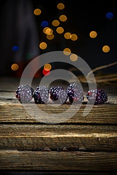 Blackberries in a row on a barn wood board with lights in the background