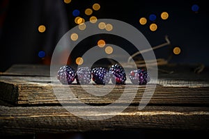 Blackberries in a row on a barn wood board with lights in the background