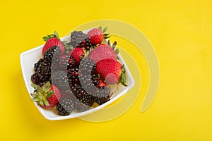 Blackberries and strawberries in a bowl on a yellow background.