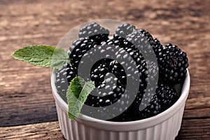 Blackberries in a white bowl with mint leaves on a wooden background close-up