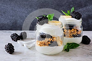 Blackberry and banana yogurt parfaits in mason jars on dark background