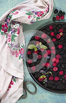 Blackberry, blueberry and raspberry on black dish with folksy scarf, flatlay