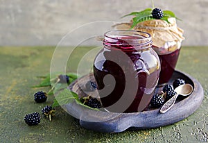 Blackberry and red currant jam in a curly glass jar on a green concrete background