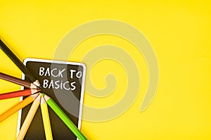 Blackboard and pencils with the text BACK TO BASICS on a yellow background, a business concept