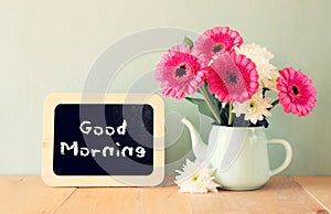 Blackboard with the phrase good morning written on it next to vase with fresh flowers