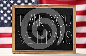 Blackboard with phrase Thank You, Veterans on white wooden table against American flag. Memorial Day