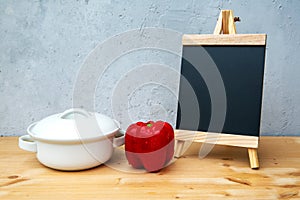 Blackboard with red bell pepper and white pot on wooden table with grey backgroundblackboard with red bell pepper and white pot on