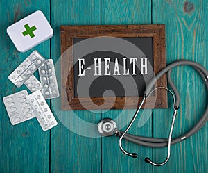 Blackboard with text & x22;E-health& x22; and stethoscope on blue wooden background