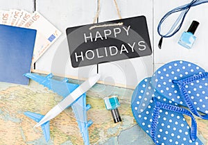 blackboard with text & x22;HAPPY HOLIDAYS& x22;, plane, map, passport, money, flops and other accessories