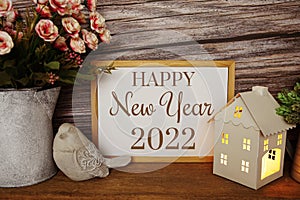 Blackboard with the text HAPPY NEW YEAR 2022 decorate with LED candle in house lantern and bird statue on wooden background
