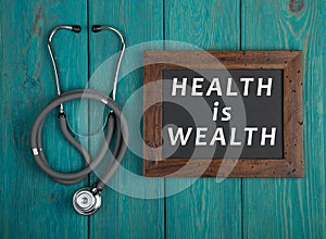 Blackboard with text & x22;Health is wealth& x22; and stethoscope on blue wooden background