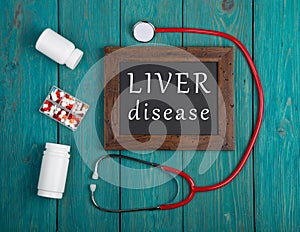 Blackboard with text & x22;Liver disease& x22;, pills and stethoscope on wooden background