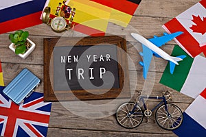 blackboard with text & x22;New Year trip& x22;, flags of different countries, airplane model, little bicycle and suitcase, compass
