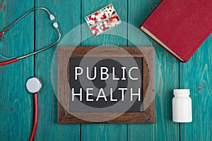 Blackboard with text & x22;Public health& x22;, pills, book and stethoscope on wooden background