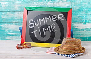 Blackboard with text it's summer time, accessories sunglasses, hat, towel on wooden deck