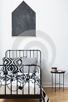 Blackboard on the wall of teenagers bedroom with black and white patterned bedding on single metal bed, real