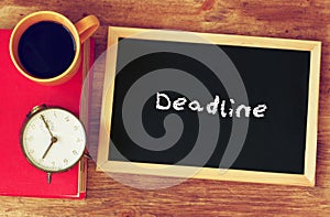 Blackboard with the word deadline written on it, clock and coffee cup over wooden board