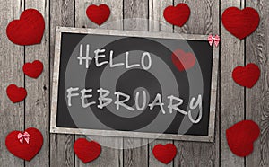 Blackboard with words hello february, surrounded by red hearts on weathered wooden background