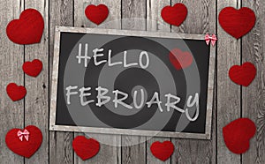 Blackboard with words hello february, surrounded by red hearts on weathered wooden background photo