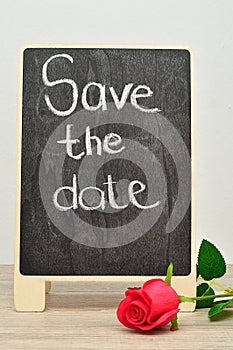 A blackboard with the words Save the date displayed with a red rose