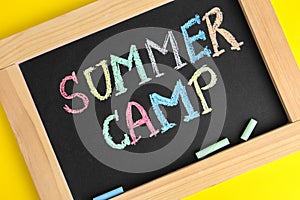 Blackboard with words SUMMER CAMP and colorful chalk on yellow background