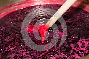 Blackcurrant jam boils in a copper basin and is stirred with a wooden spoon