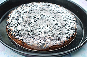 Blackcurrant tart with sugar powder on a round baking tray