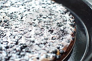 Blackcurrant tart with sugar powder on a round baking tray