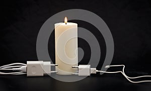 Blackout concept. Electric charger with cable near lighting candle on dark background