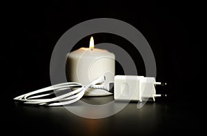 Blackout concept. Electric charger with cable near lighting candle on dark background