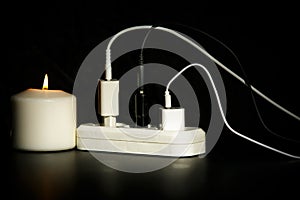 Blackout concept. Electric charger with cable near lighting candle on dark background