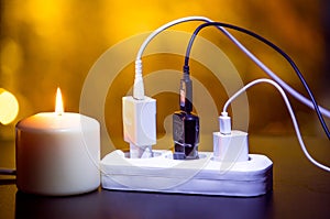 Blackout concept. Electric charger with cable near lighting candle on dark background