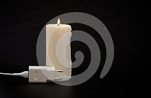 Blackout concept. Electric charger with cable near lighting candle on dark background